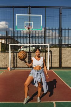 Woman standing confidently with a basketball on an outdoor court in casual attire.