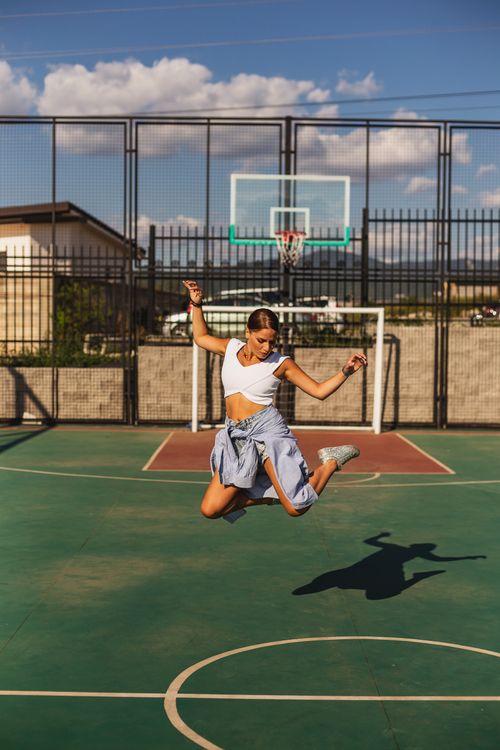 Free Young woman jumping energetically on an outdoor basketball court on a sunny day. Stock Photo