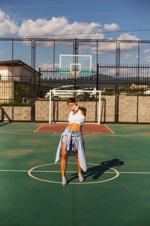 Free Woman in casual outfit poses on outdoor basketball court, sunny day vibe. Stock Photo