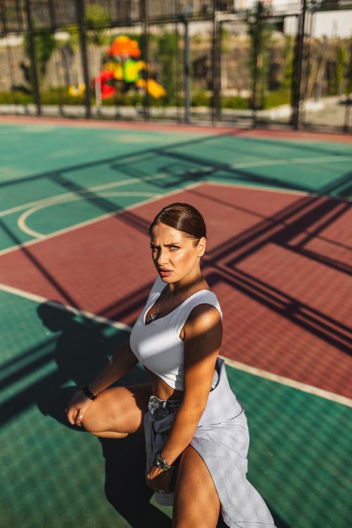 Free A woman confidently poses on an outdoor basketball court in bright sunlight. Stock Photo