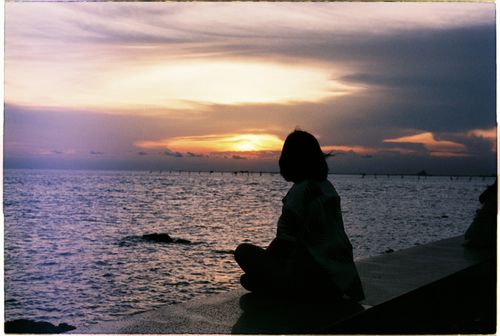 Free A peaceful sunset over the ocean in Vũng Tàu, Vietnam, with a woman sitting in the foreground. Stock Photo