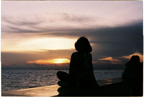 Free A serene silhouette of a woman sitting by the sea during sunset, capturing tranquility and beauty. Stock Photo