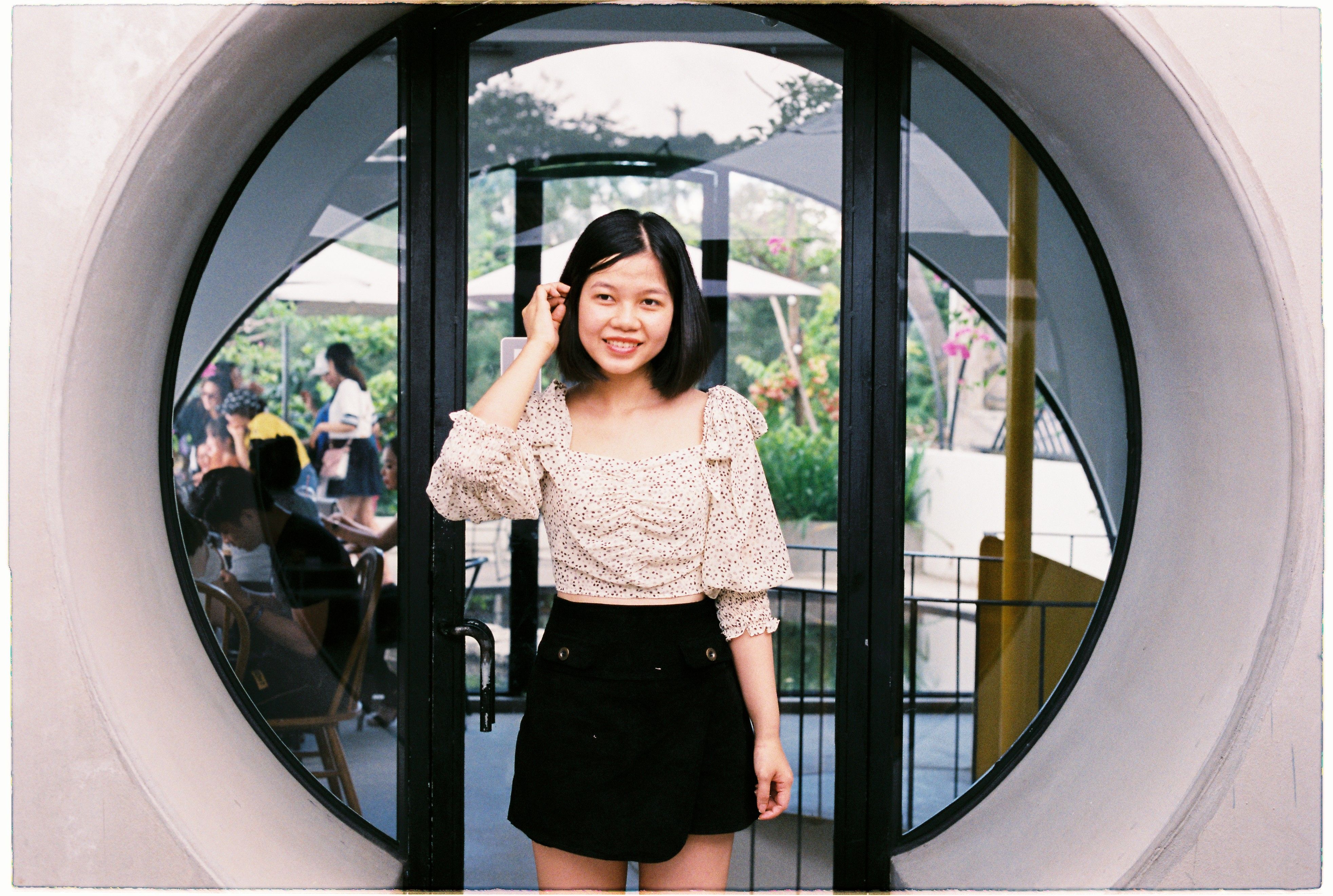 A cheerful woman in a stylish blouse smiles while posing in a circular doorway.