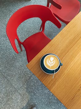 Artistic latte in a chic café setting with red chairs and wooden table.