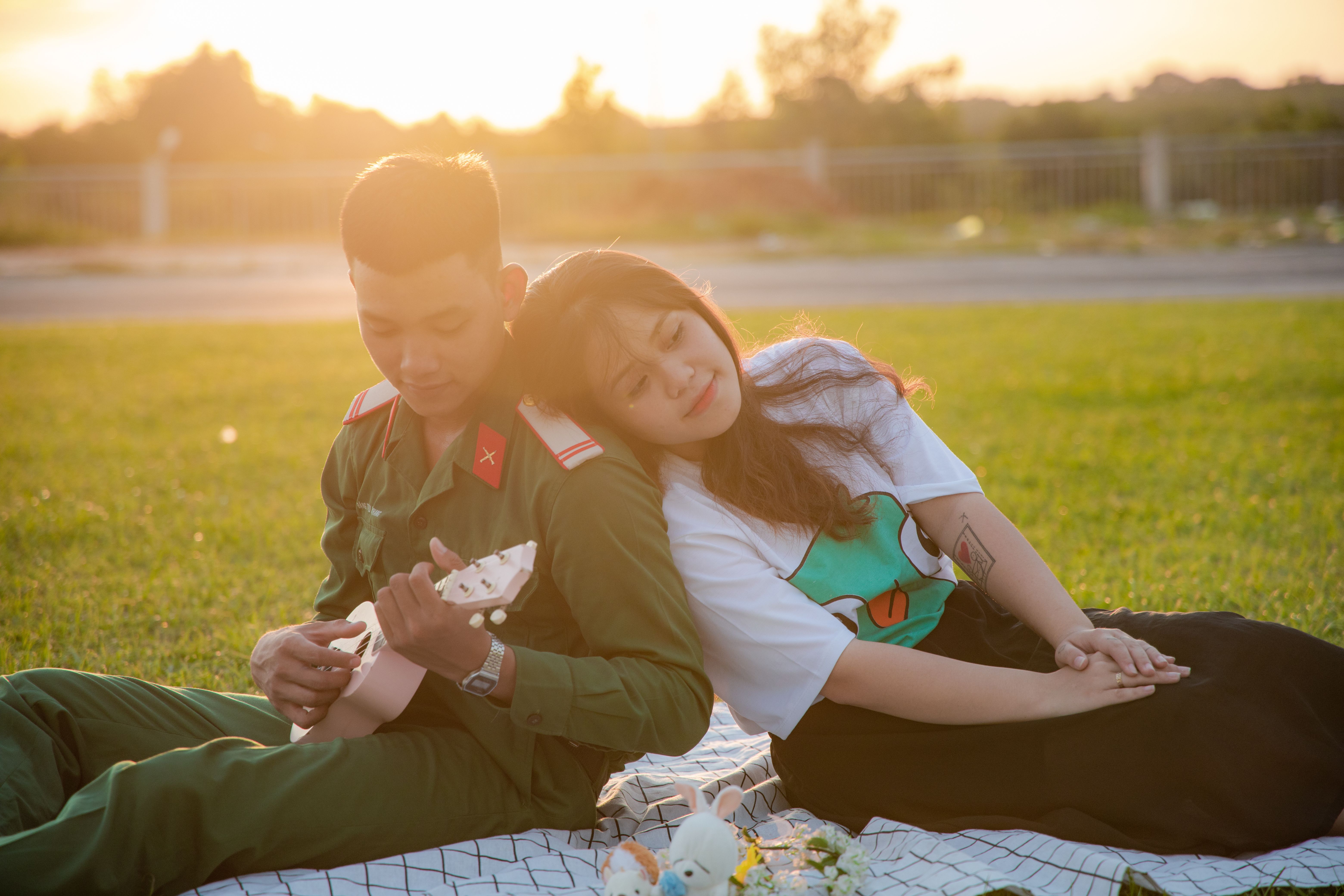 A couple enjoying a sunny day in the park, playing ukulele and relaxing on grass.