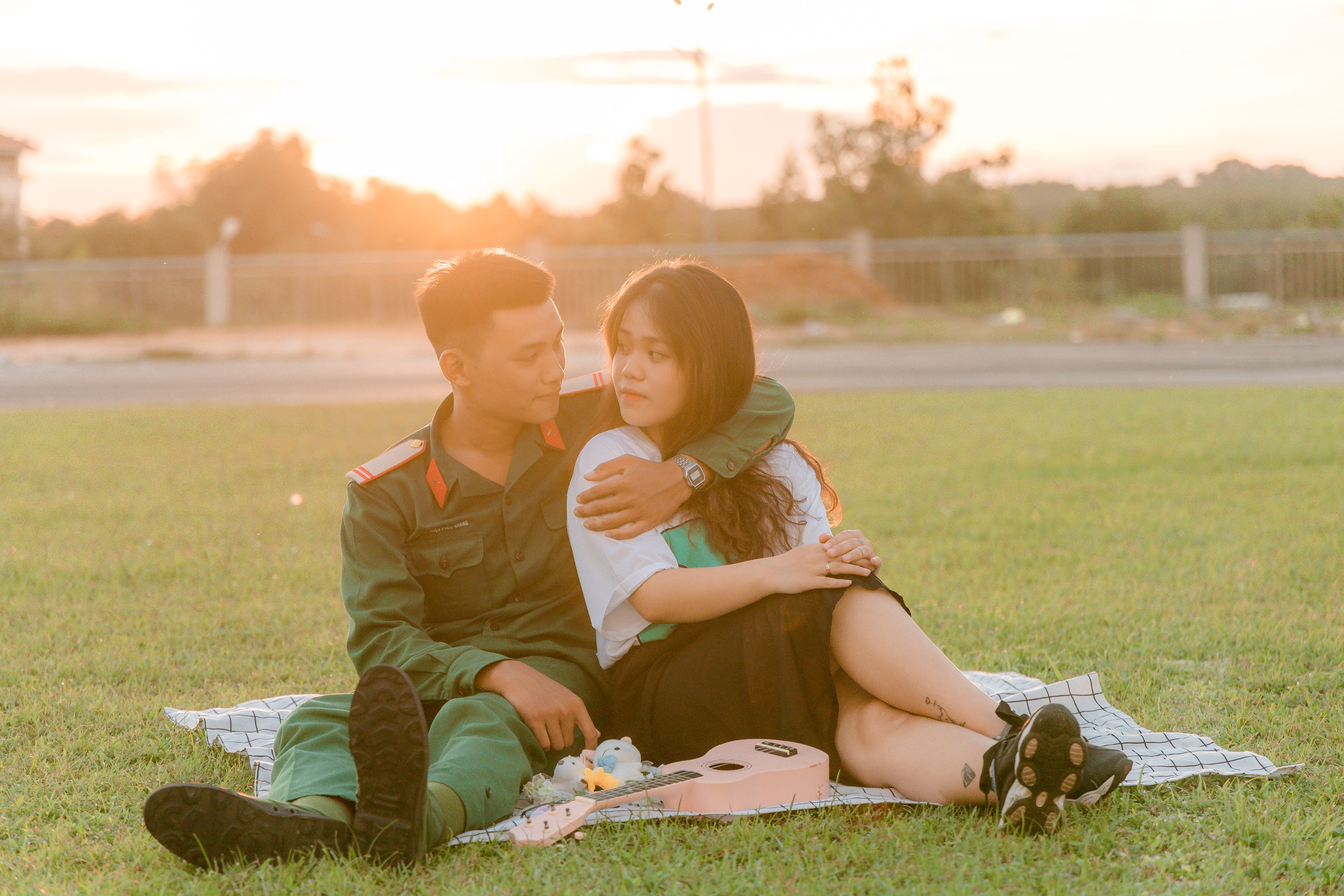 A couple shares a tender moment sitting on a blanket during a sunset picnic outdoors.