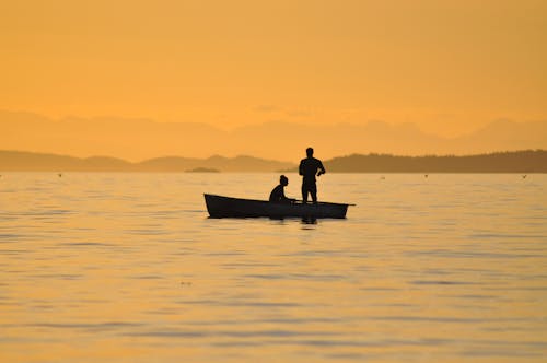 Gratis 2 Orang Berdiri Duduk Di Perahu Di Perairan Foto Stok