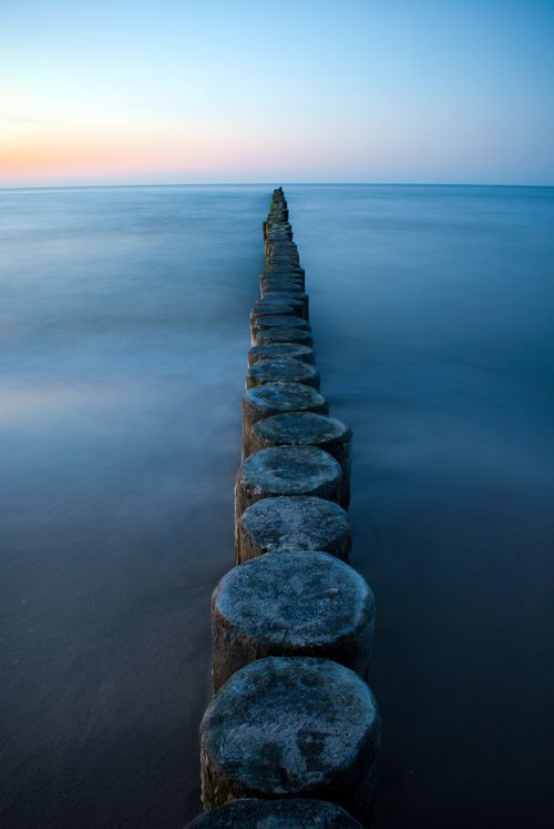 Free Captivating view of ocean groynes leading into the calm sea at sunset, capturing nature's tranquility. Stock Photo