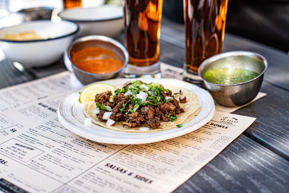 A white bowl layered with cilantro-lime rice, seasoned ground beef, black beans, corn, shredded lettuce, diced tomato, cheese, and a dollop of sour cream, with a lime wedge on the side.