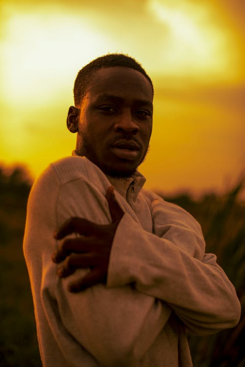 African American male in warm clothes grabbing hands and standing in field while looking at camera