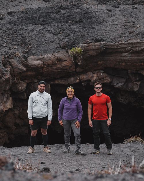 Free Group of multiethnic travelers in comfortable outfits standing on rocky slope near stone cave and looking at camera Stock Photo
