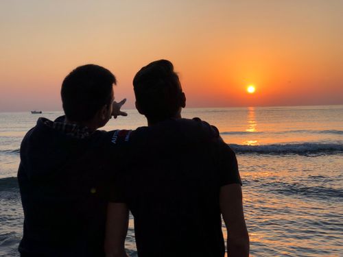 Free Back view of faceless friends standing on coast near water and hugging while looking at bright sundown Stock Photo