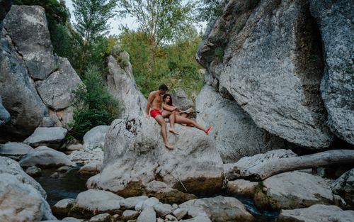Free Full body of fit couple sitting together on stone in rocky terrain and enjoying summer Stock Photo