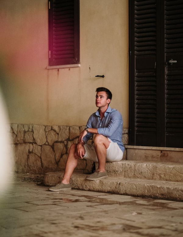 Young man sitting on old stone stairs beside a shuttered wall — photo by Andrea Bosco on Pexels
