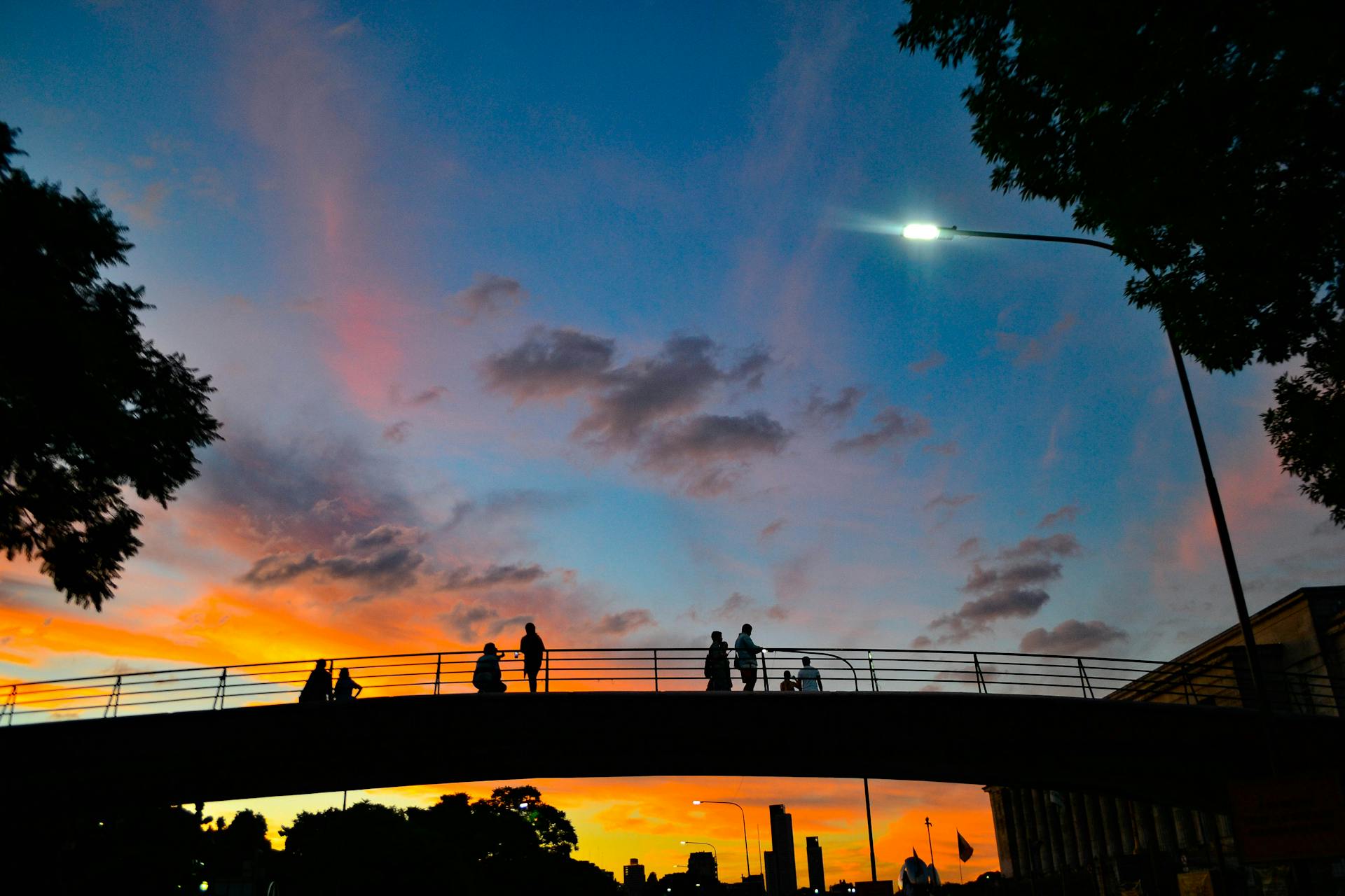A scenic silhouette of people on a bridge against a vibrant sunset sky in San Nicolas, Argentina.