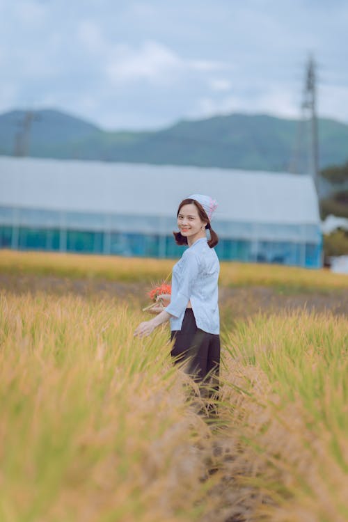Woman in White Long Sleeve Shirt and Brown Pants Standing on Rice Field