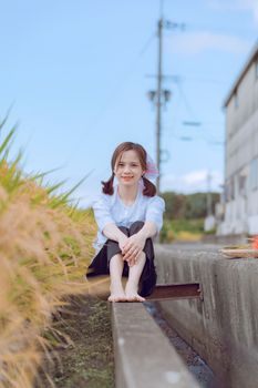 Happy young girl sitting barefoot outdoors, enjoying a sunny day in a rural setting.