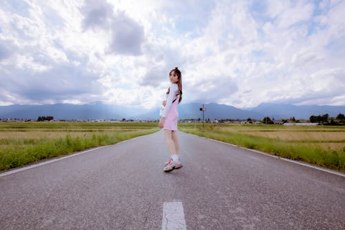 Woman in Pink and White Dress Standing on a Gray Asphalt Road