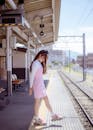 Woman in White Long Sleeve Shirt and Pink Jumper Dress Standing on a Train Station