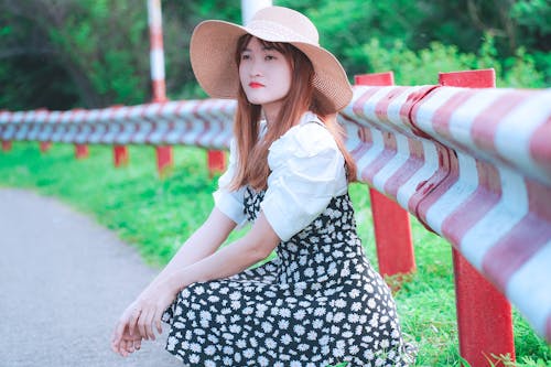 Free Woman in White and Black Dress Wearing Brown Hat Sitting on Red and White Striped Bench Stock Photo