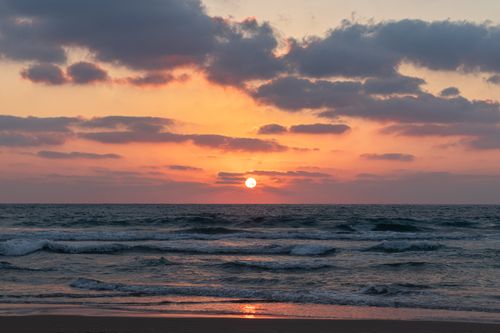 Free Picturesque scenery of waving sea washing sandy under cloudy colorful sky with horizon and sun at sunrise Stock Photo
