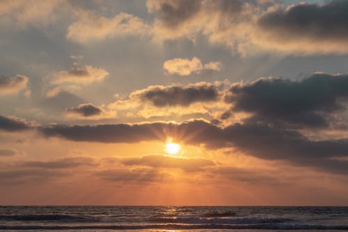 Picturesque scenery of waving sea under colorful cloudy sky with shiny sun rays at dawn