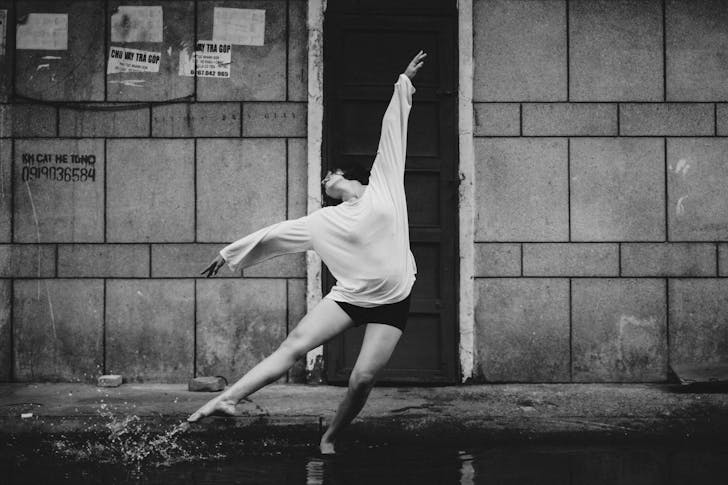 Black and white full body of graceful ballerina dancing on street in splashing water