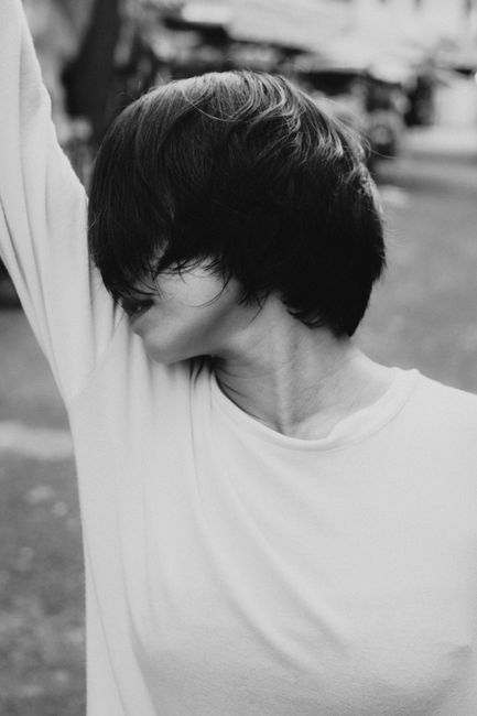 Black and white calm faceless female hiding face with hair while standing on street with hand raised