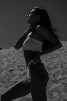 一位优雅女子身着泳衣，在阳光明媚的沙丘上梦幻般地摆出姿势，拥抱着宁静的时刻