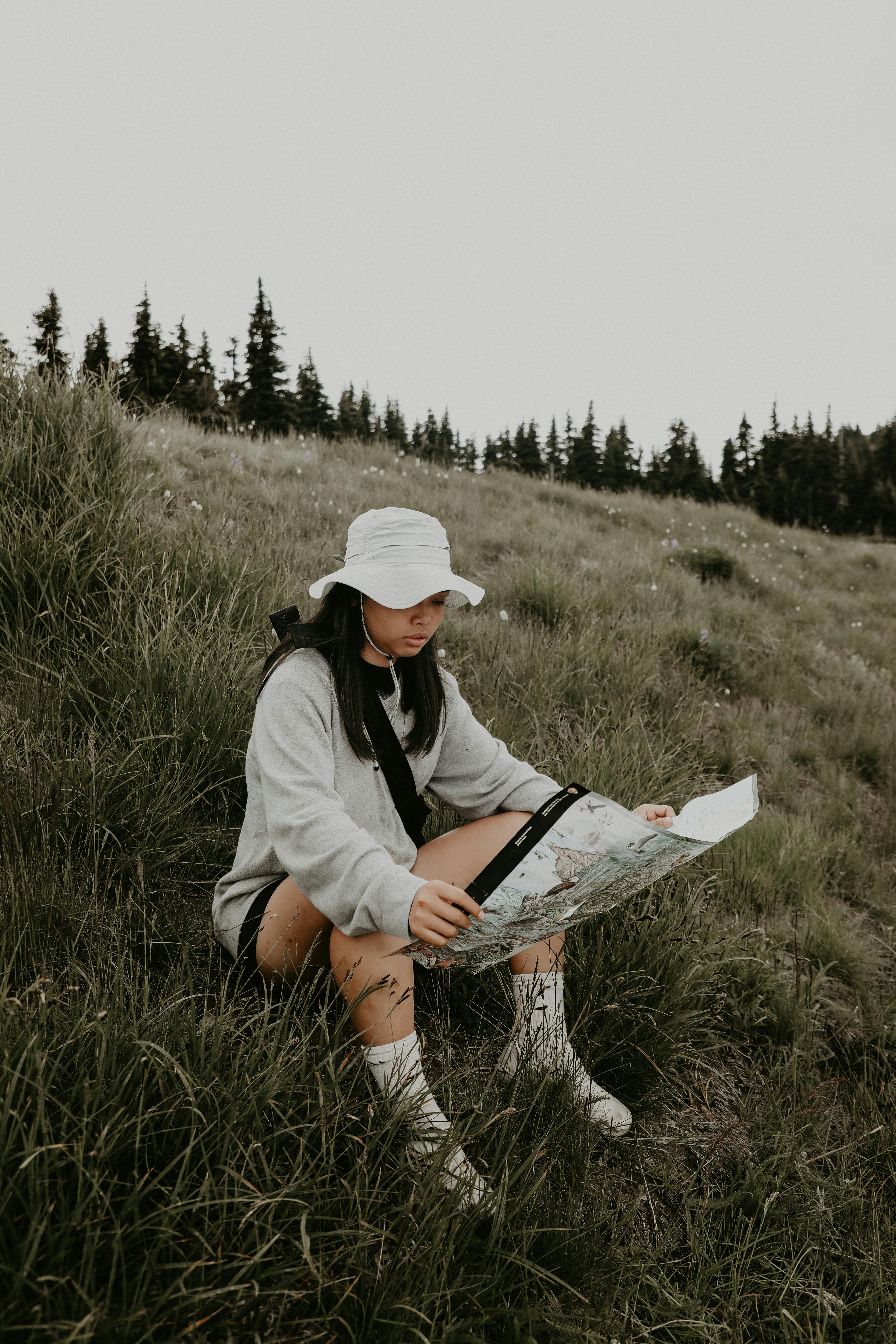 Full body of traveler in panama sitting on green grassy slope and reading map