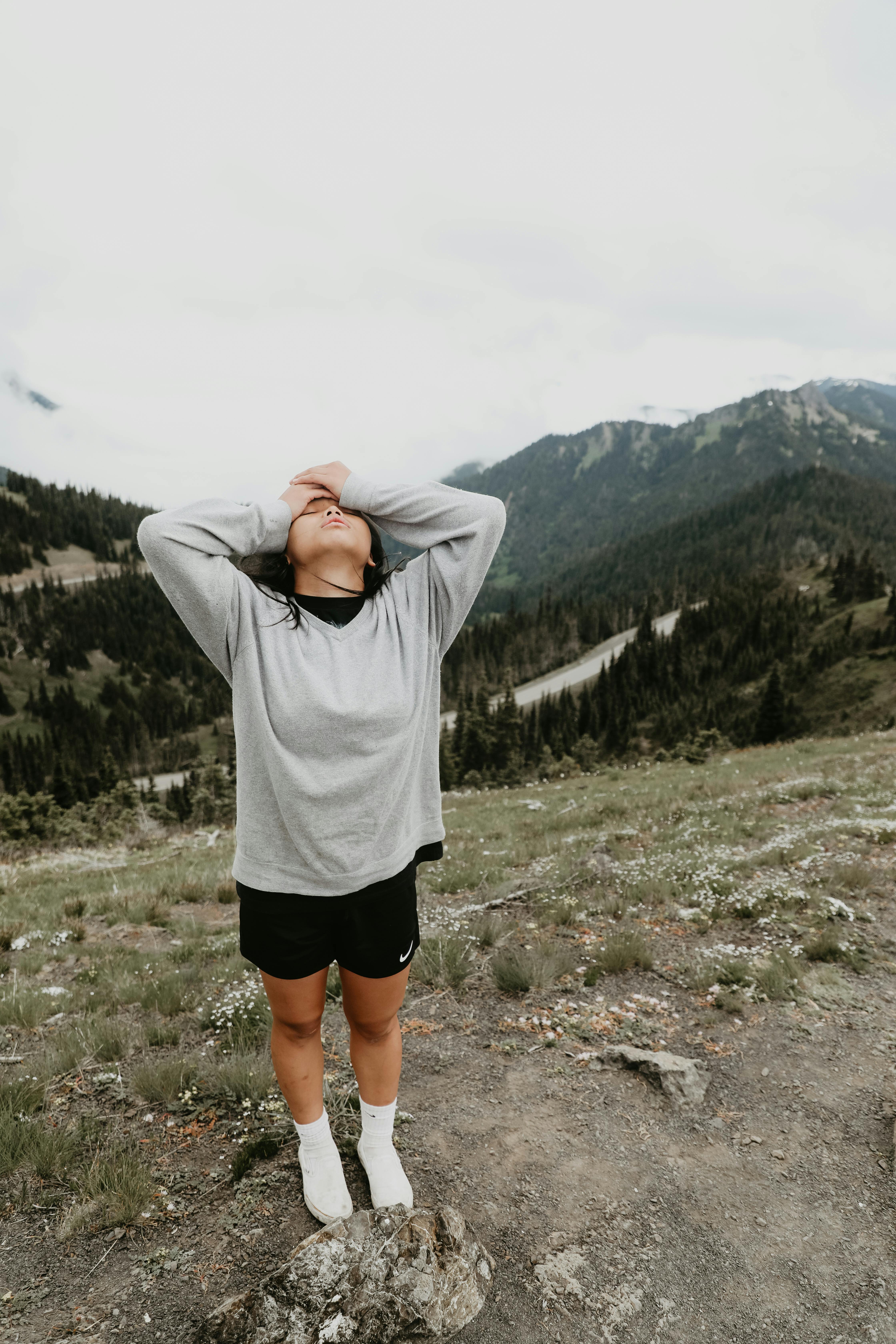 Full body of female hiker in sportswear standing on top of hill and holding hands on head