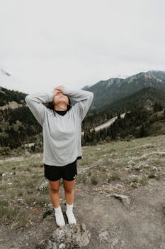 Full body of female hiker in sportswear standing on top of hill and holding hands on head