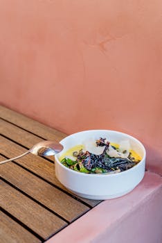 A tantalizing dish served in a ceramic bowl, placed on a wooden surface beside a pink wall.