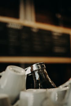 Collection of white ceramic cups heaped on counter against blurred menu boards in coffee house