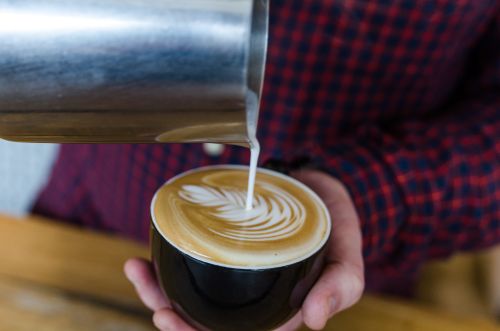 Free Close-up of a barista pouring milk to create beautiful latte art in a coffee cup. Stock Photo