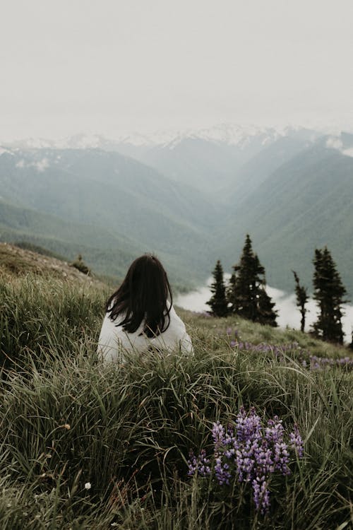 Unrecognizable woman sitting on hill and looking at majestic mountains