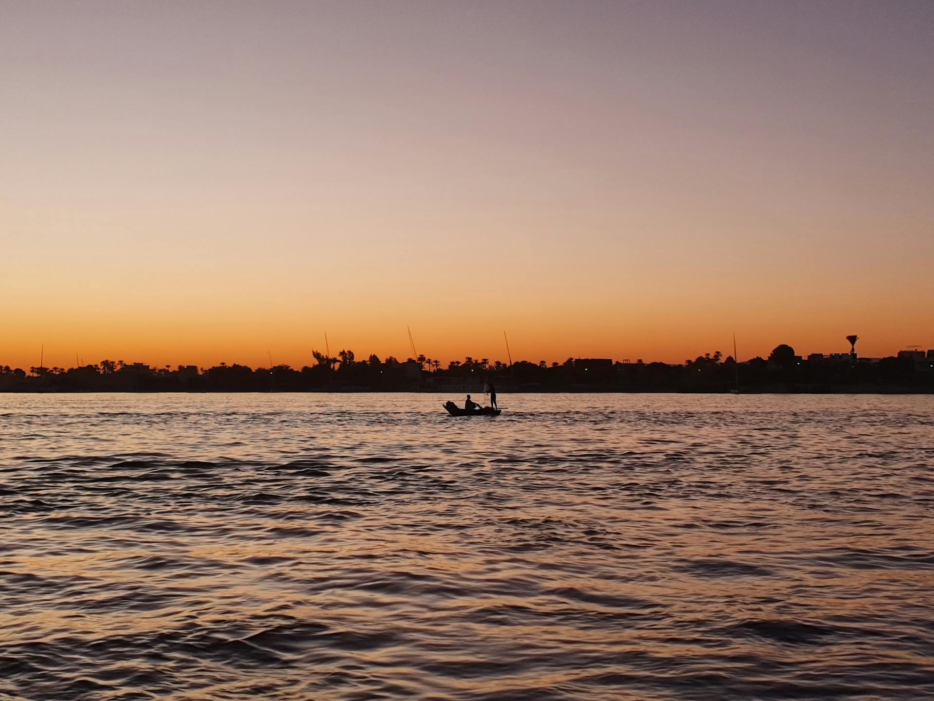 Peaceful boat silhouette on the Nile at sunset, capturing the tranquil Egyptian landscape.