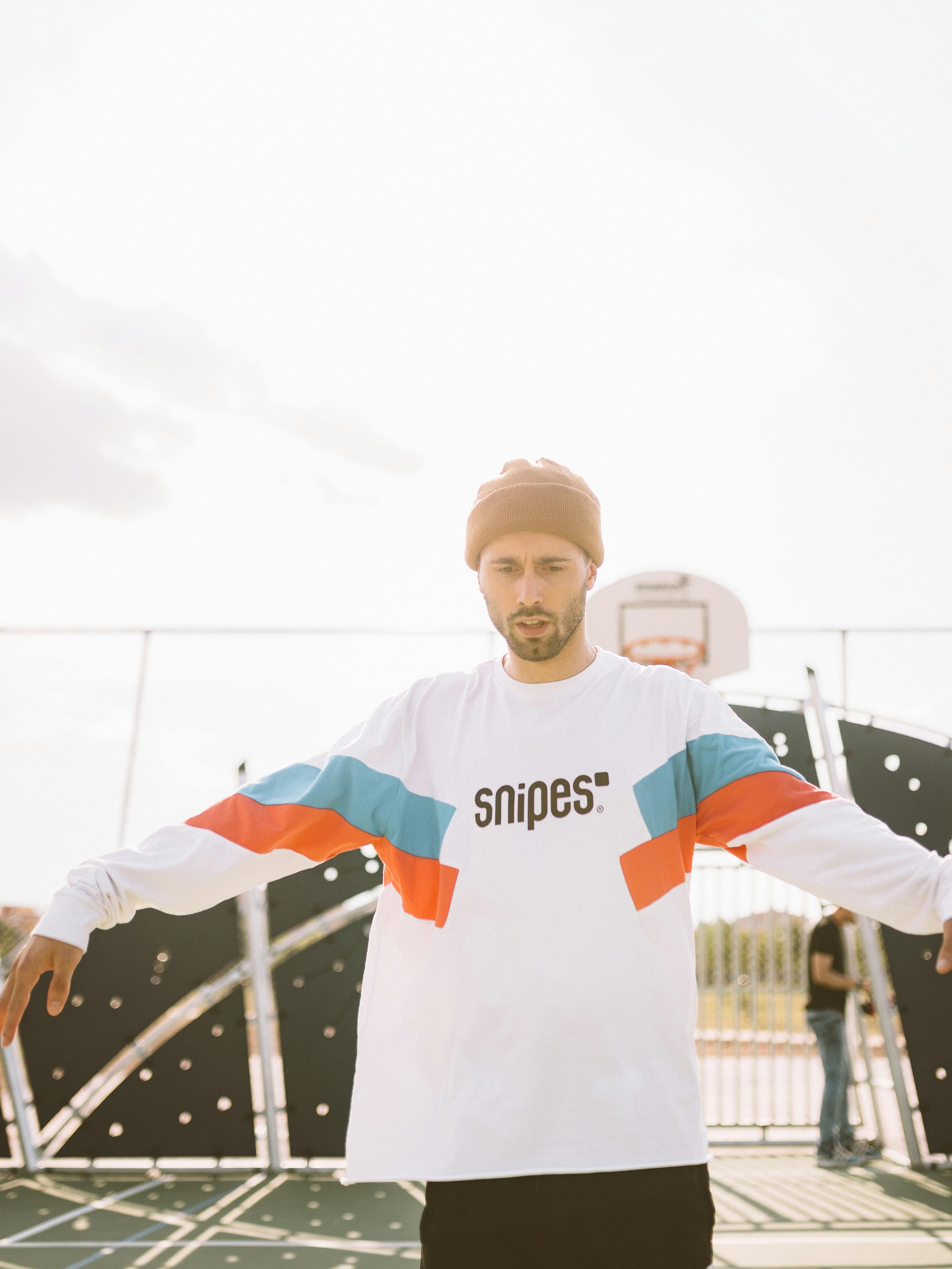 Man in a colorful sweater outdoors near a basketball court, emphasizing streetwear fashion.