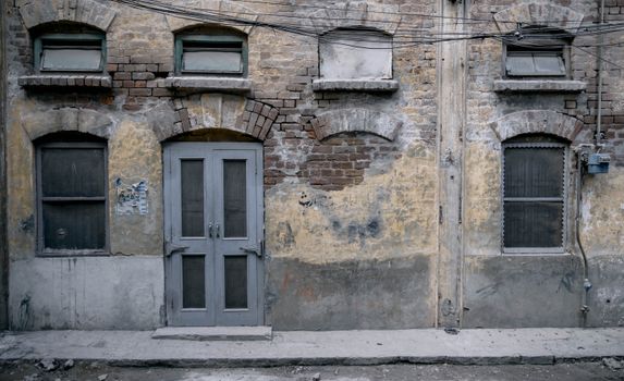 Aged brick facade with old windows and doorway in Faisalabad, Pakistan.