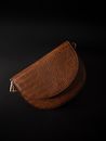 Top view classy brown leather purse of oval shape placed on black surface in studio