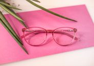 Eyeglasses on pink surface near houseplant leaves