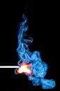 在黑色背景下，一根火柴点燃了充满活力的蓝色烟雾