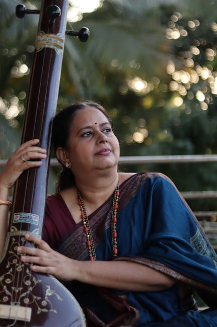 Indian woman in a saree with a traditional musical instrument outdoors, conveying culture and tranquility.