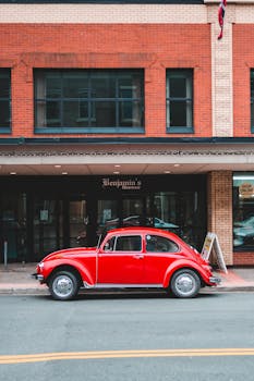 Classic red automobile parked outside a brick building on an urban street.