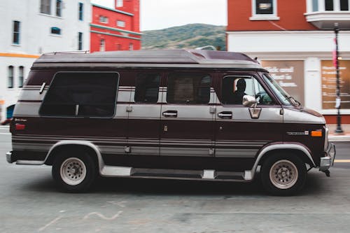 Side view of big black car riding on asphalt roadway on city street along residential buildings with blurred background outside