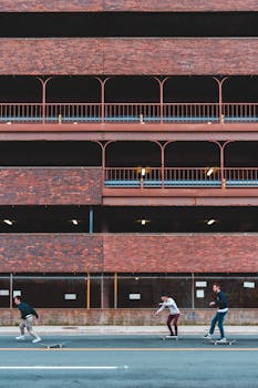 Exterior of construction with brick wall and metal fence located on street near road with men riding on skateboards in city