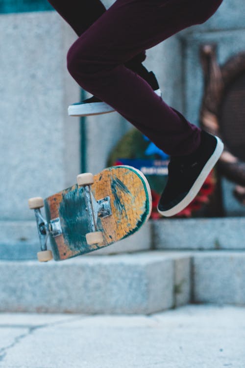 Unrecognizable male leaping up on skateboard near concrete column while performing trick in city street during practicing on blurred background