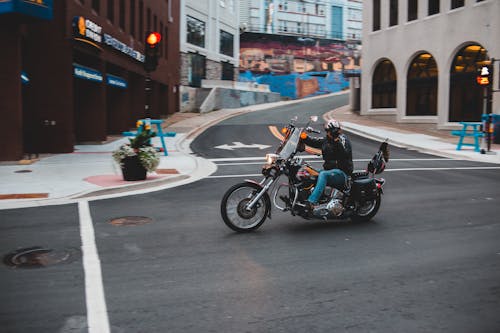 Full body of unrecognizable male biker in helmet riding motorbike on asphalt road near buildings and crossroad in city street outside