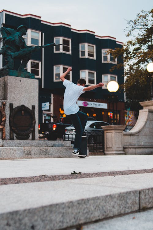 Full body of unrecognizable male with raised arms performing trick on skateboard while practicing skills on concrete square in city street