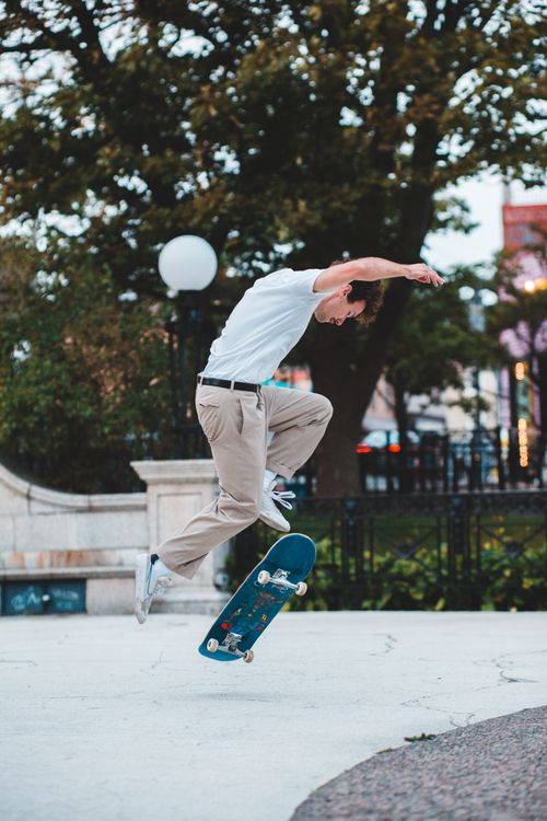 Free Full body of anonymous male skateboarder performing leap trick on skateboard while training in park with green trees in city street Stock Photo